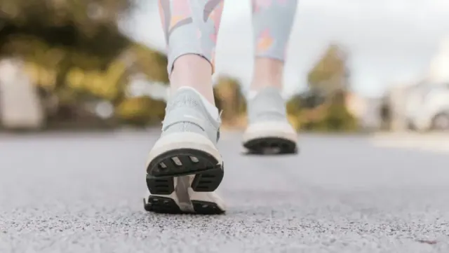 A close-up of a person’s athletic shoes as they walk on a road.